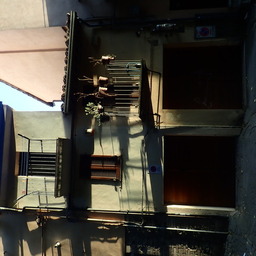 ordinary house in very oblique summer evening light; on one of the two balconies there are some plants, some of which dry