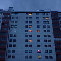 part of a huge apartment complex I'd rather live in than have to look at every day, yet at dusk it can look interesting: both walls and sky look blue-gray, but some windows are lit in different warm tones of yellow, orange and purple