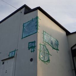 the corner of a building whose plaster is falling apart; each spot where it has come off is covered in a thin layer of blue semi-transparent plastic, held in place by some dark green tape