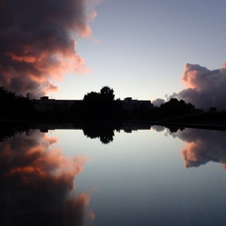 perfect reflection of some backlit houses and trees; the sky behind is blue with pink clouds