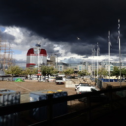 messy cityscape under a dramatic black sky with a white seagull against it; various landmarks are visible in the background but the foreground is some kind of construction site