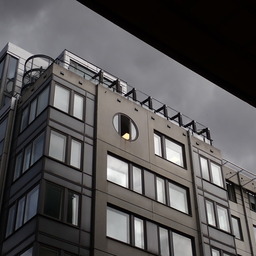 unremarkable modern building that is suddenly made more interesting by the light conditions: everything is different shades of gray, but inside a window there's some yellow light