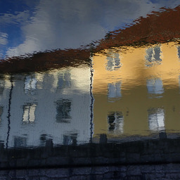 a white and a yellow three-floor houses reflected on the rippled surface of the water of a canal