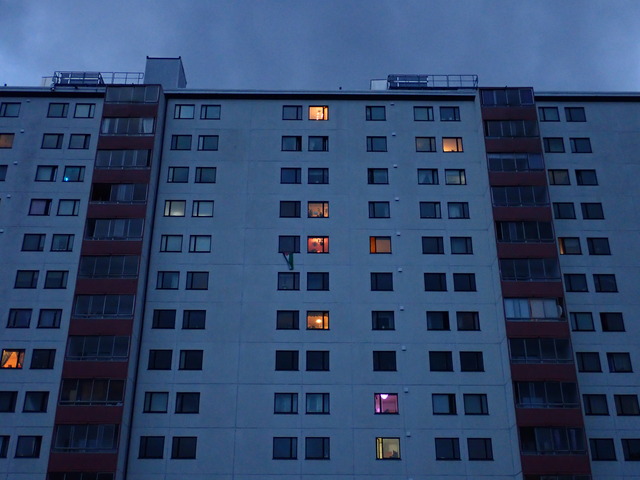part of a huge apartment complex I'd rather live in than have to look at every day, yet at dusk it can look interesting: both walls and sky look blue-gray, but some windows are lit in different warm tones of yellow, orange and purple