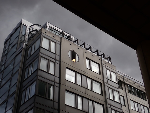 unremarkable modern building that is suddenly made more interesting by the light conditions: everything is different shades of gray, but inside a window there's some yellow light