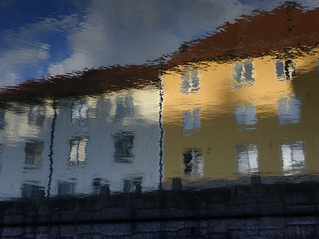 a white and a yellow three-floor houses reflected on the rippled surface of the water of a canal